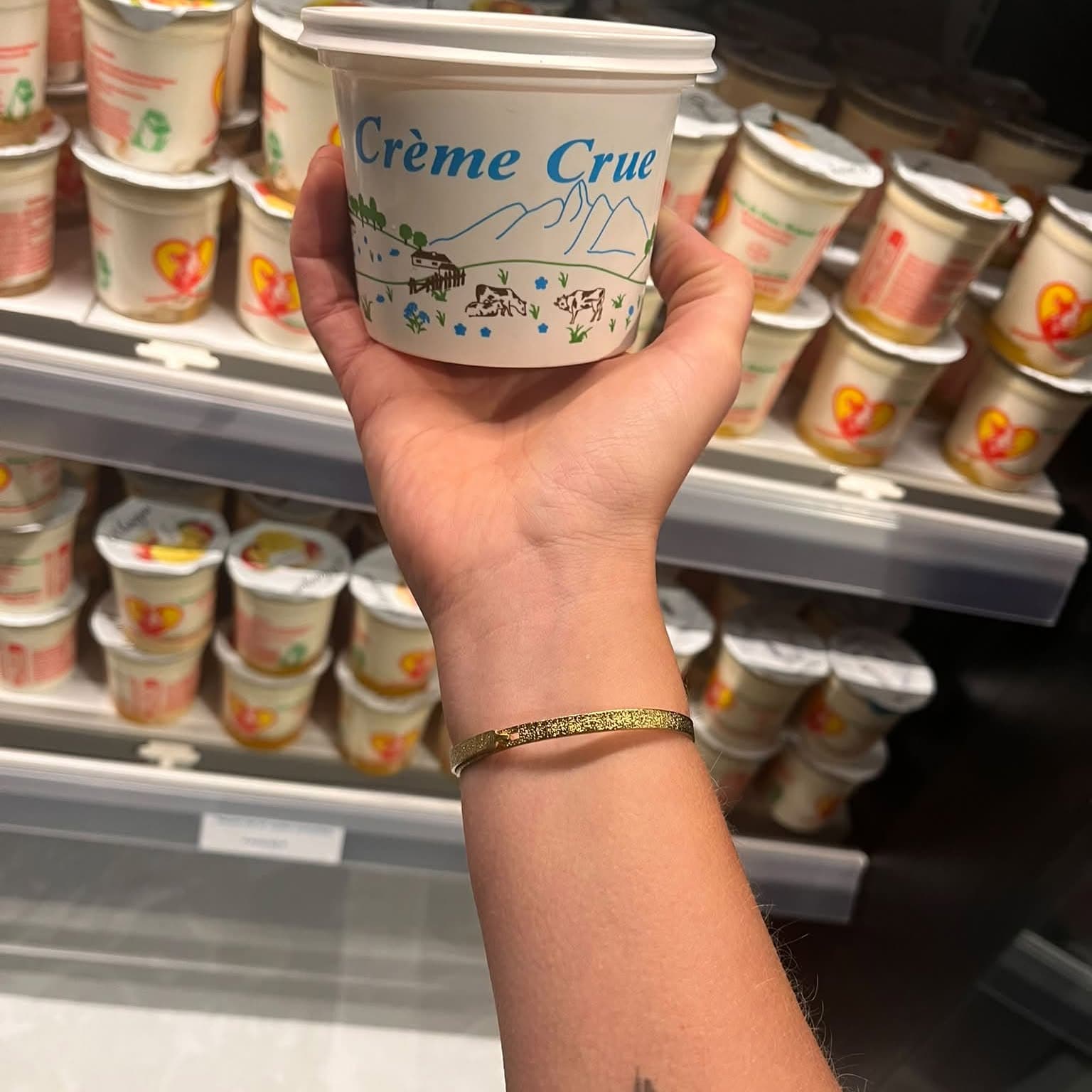 Un pot de crème crue de la ferme tenu devant le rayon frais